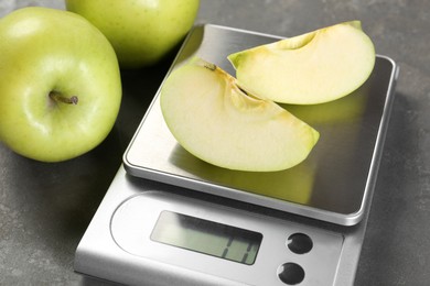 Photo of Kitchen scale with pieces of apple and fruits on grey textured table, closeup