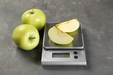 Photo of Kitchen scale with pieces of apple and fruits on grey textured table