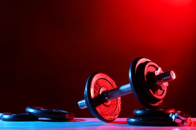 Photo of Barbell and parts of one on table in color lights. Space for text