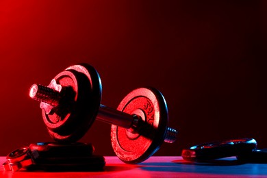 Photo of Barbell and parts of one on table in color lights. Space for text