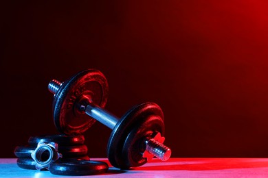 Photo of Barbell and parts of one on table in color lights. Space for text