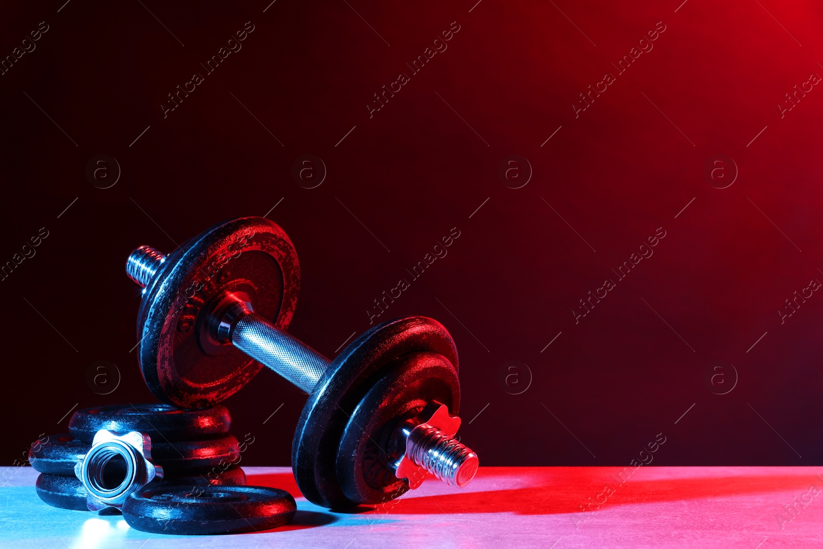 Photo of Barbell and parts of one on table in color lights. Space for text