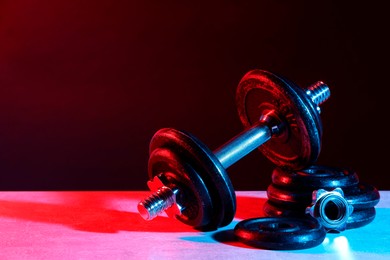 Photo of Barbell and parts of one on table in color lights. Space for text