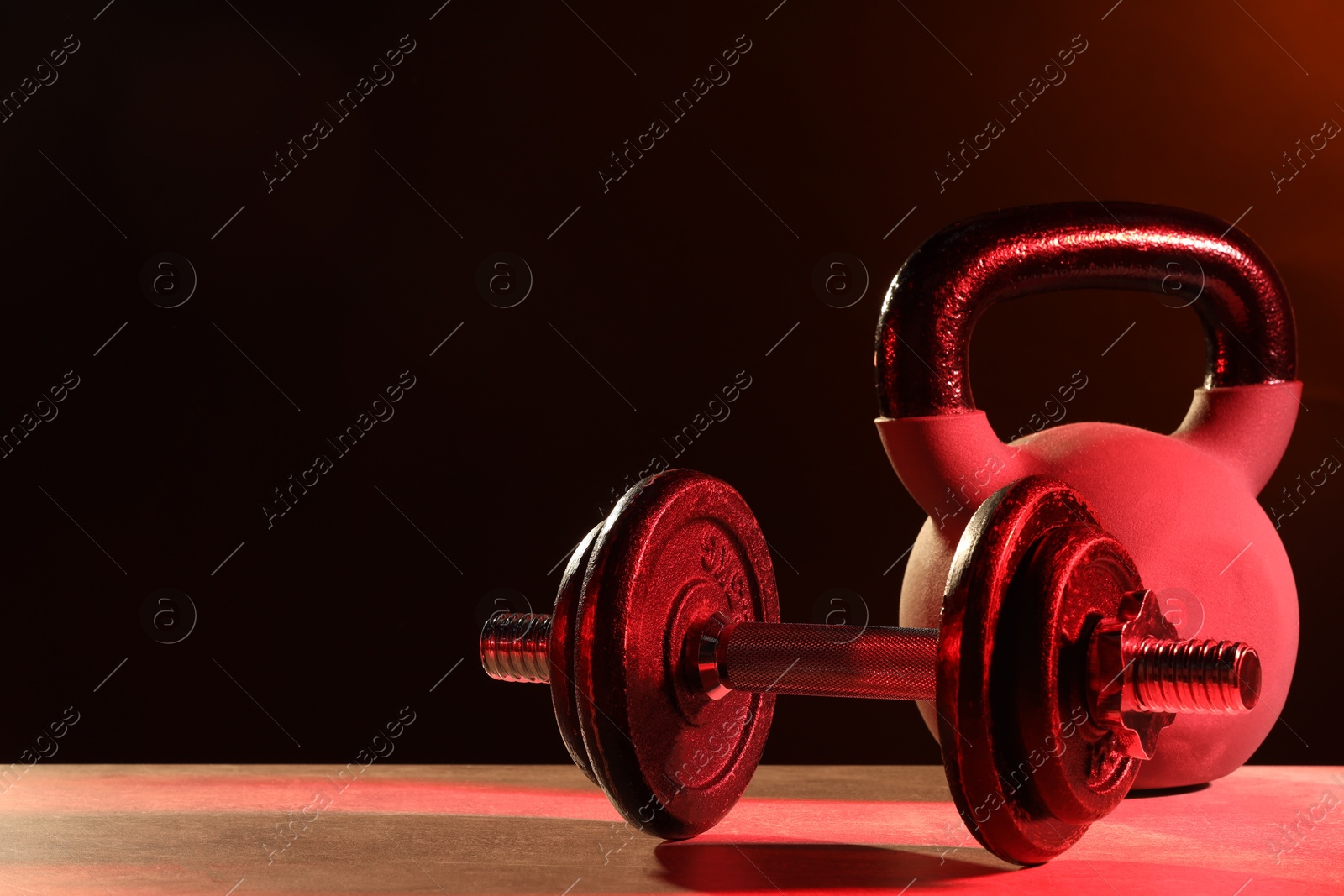 Photo of Barbell and kettlebell on table in color lights. Space for text