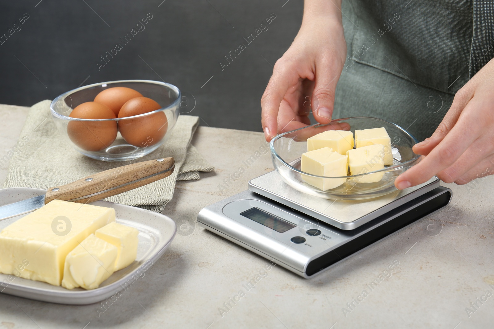 Photo of Woman weighing butter on kitchen scale at grey table, closeup