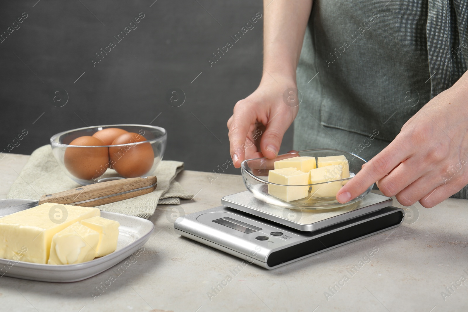 Photo of Woman weighing butter on kitchen scale at grey table, closeup