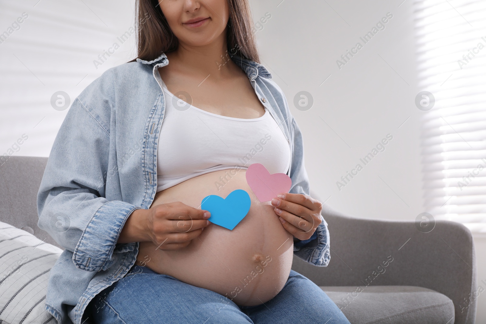 Photo of Pregnant woman with paper hearts on sofa at home, closeup. Expecting twins