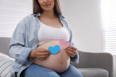 Photo of Pregnant woman with paper hearts on sofa at home, closeup. Expecting twins