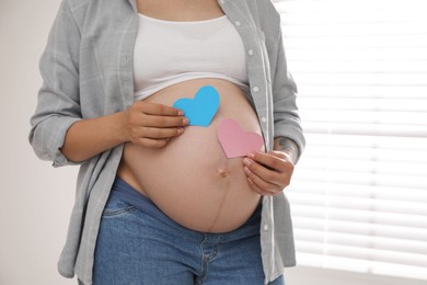 Photo of Pregnant woman with paper hearts at home, closeup. Expecting twins