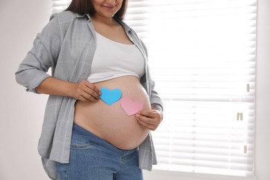 Photo of Pregnant woman with paper hearts at home, closeup. Expecting twins