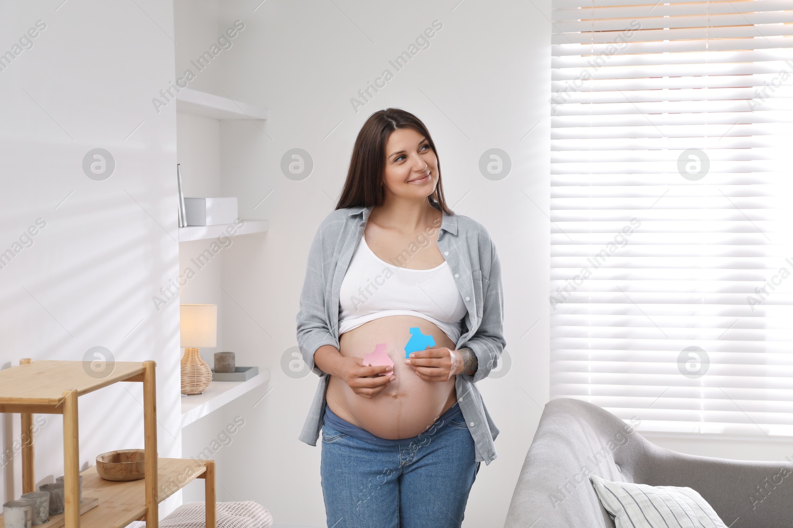 Photo of Beautiful pregnant woman with paper T-shirts at home. Expecting twins