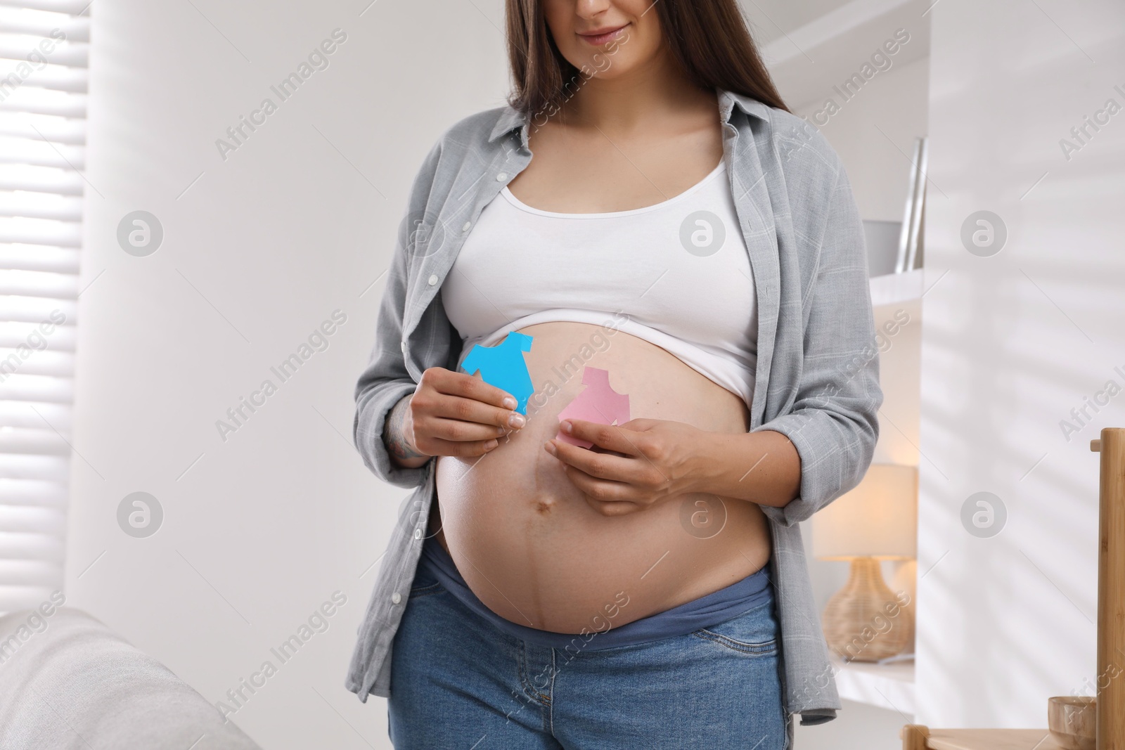 Photo of Pregnant woman with paper T-shirts at home, closeup. Expecting twins