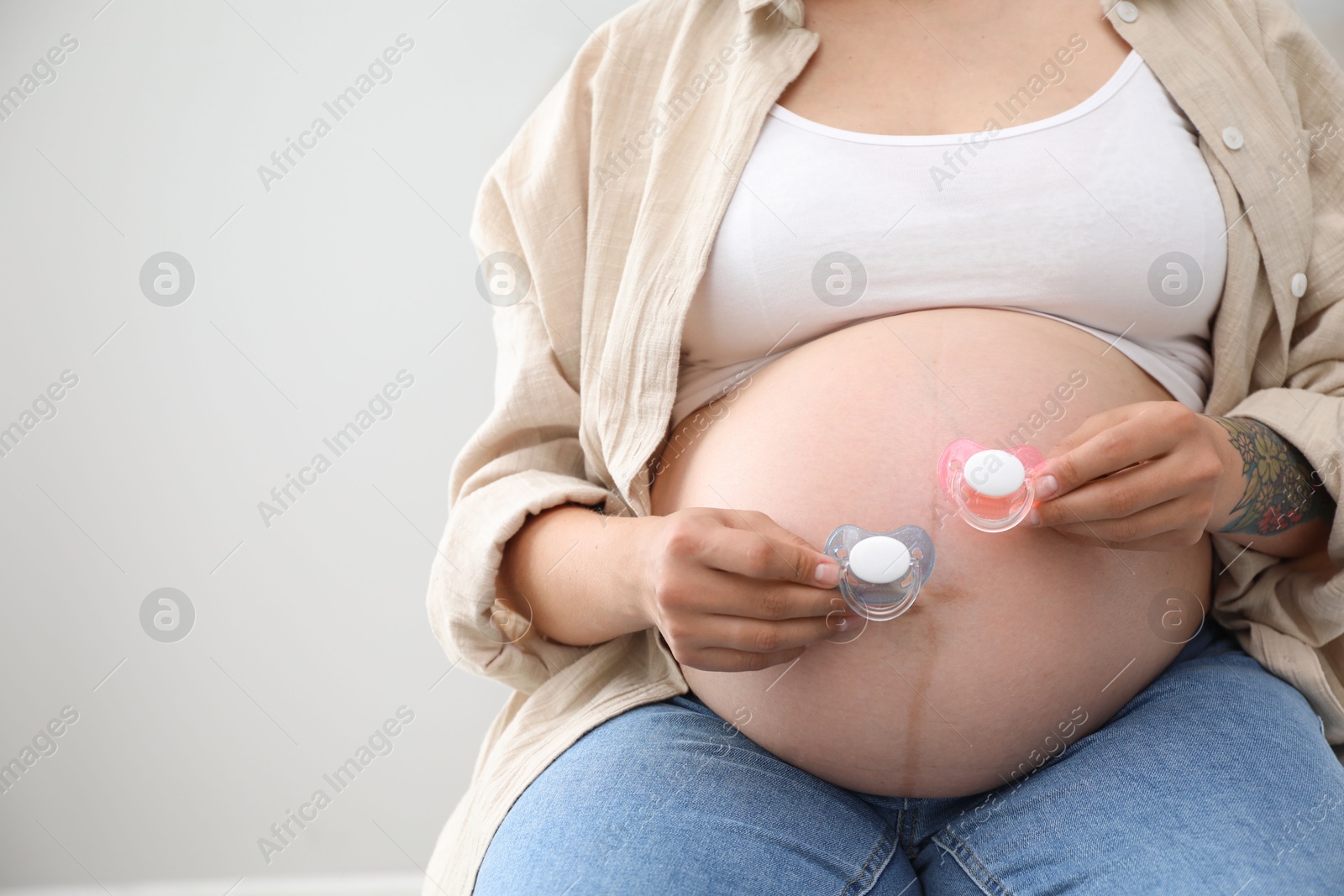 Photo of Pregnant woman with pacifiers on light gray background, closeup and space for text. Expecting twins