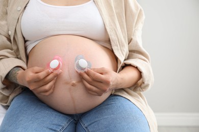 Photo of Pregnant woman with pacifiers on light gray background, closeup. Expecting twins