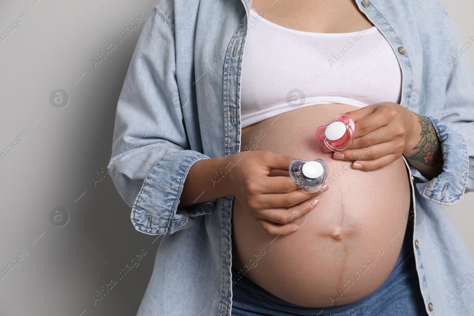 Photo of Pregnant woman with pacifiers on light gray background, closeup. Expecting twins