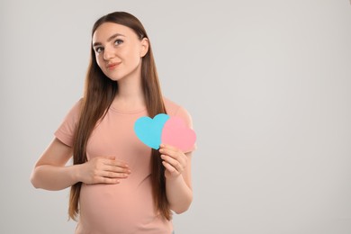 Photo of Expecting twins. Pregnant woman holding two paper cutouts of hearts on light grey background, space for text