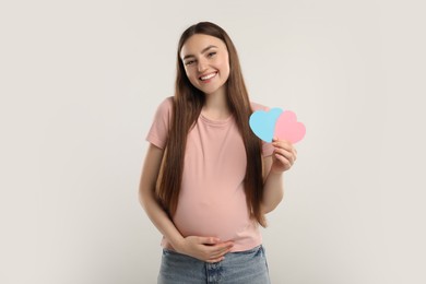 Photo of Expecting twins. Pregnant woman holding two paper cutouts of hearts on light grey background