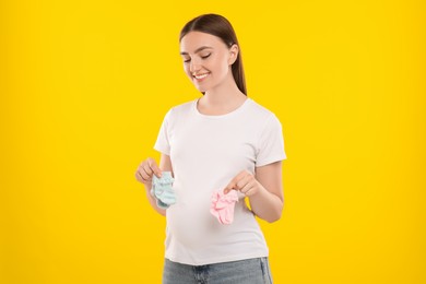 Photo of Expecting twins. Pregnant woman holding two pairs of socks on yellow background