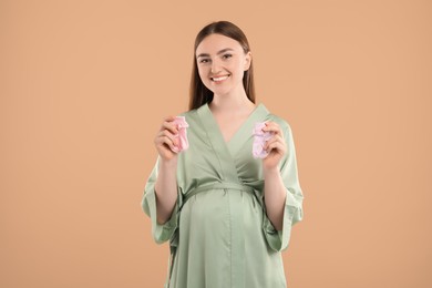 Photo of Expecting twins. Pregnant woman holding two pairs of socks on light brown background