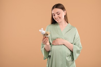 Photo of Expecting twins. Pregnant woman holding two toys on light brown background, space for text