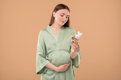 Photo of Expecting twins. Pregnant woman holding two toys on light brown background