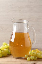 Tasty juice in glass jug and fresh grapes on wooden table