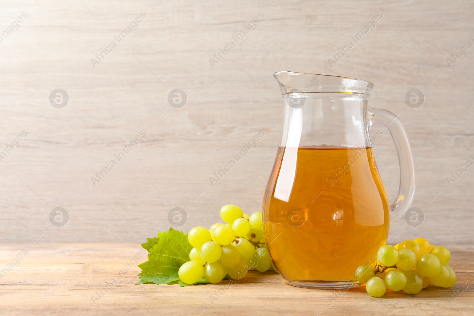 Photo of Tasty juice in glass jug and fresh grapes on wooden table, space for text