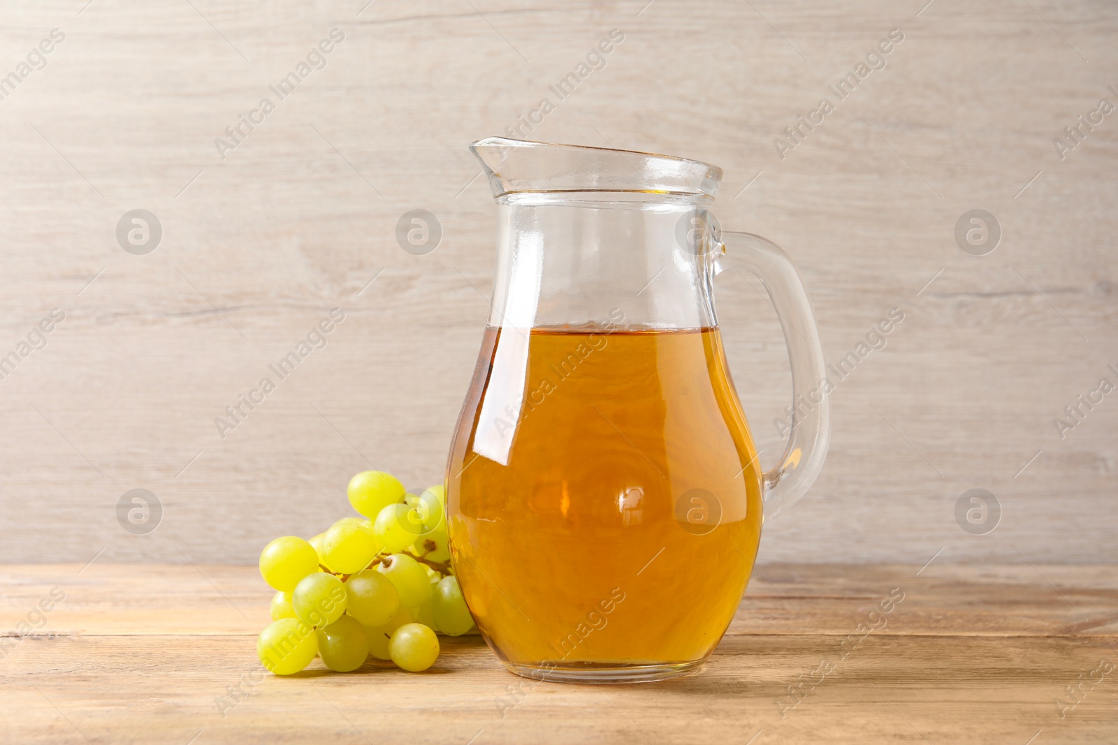 Photo of Tasty juice in glass jug and fresh grapes on wooden table