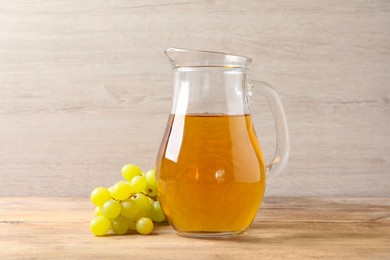 Tasty juice in glass jug and fresh grapes on wooden table