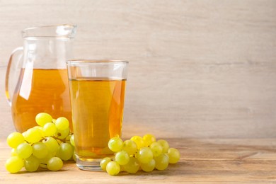 Photo of Tasty juice in glass, jug and fresh grapes on wooden table, space for text