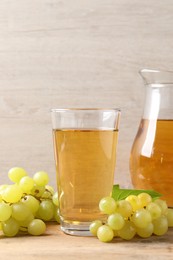 Tasty juice in glass, jug and fresh grapes on wooden table