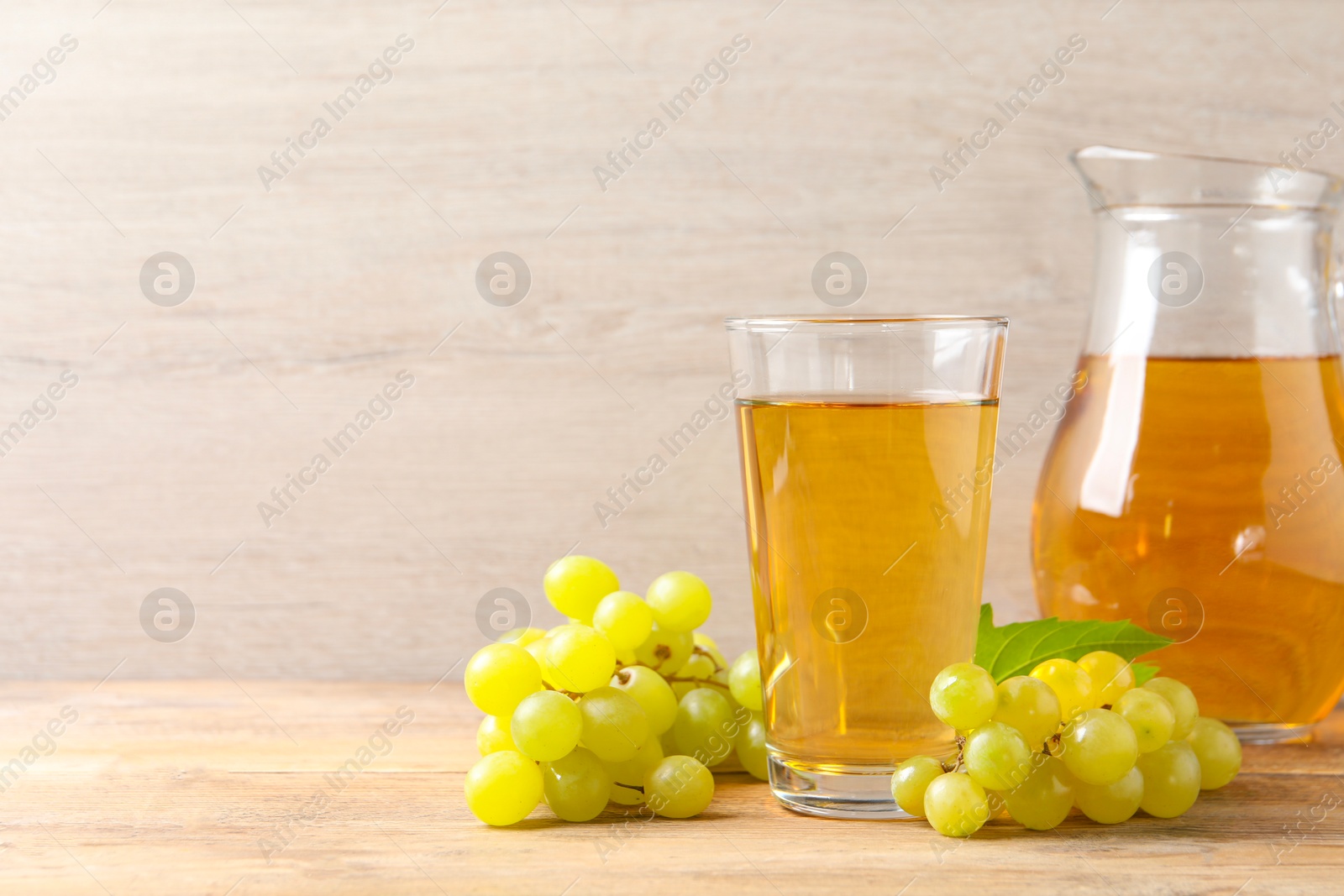 Photo of Tasty juice in glass, jug and fresh grapes on wooden table, space for text