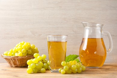 Tasty juice in glass, jug and fresh grapes on wooden table