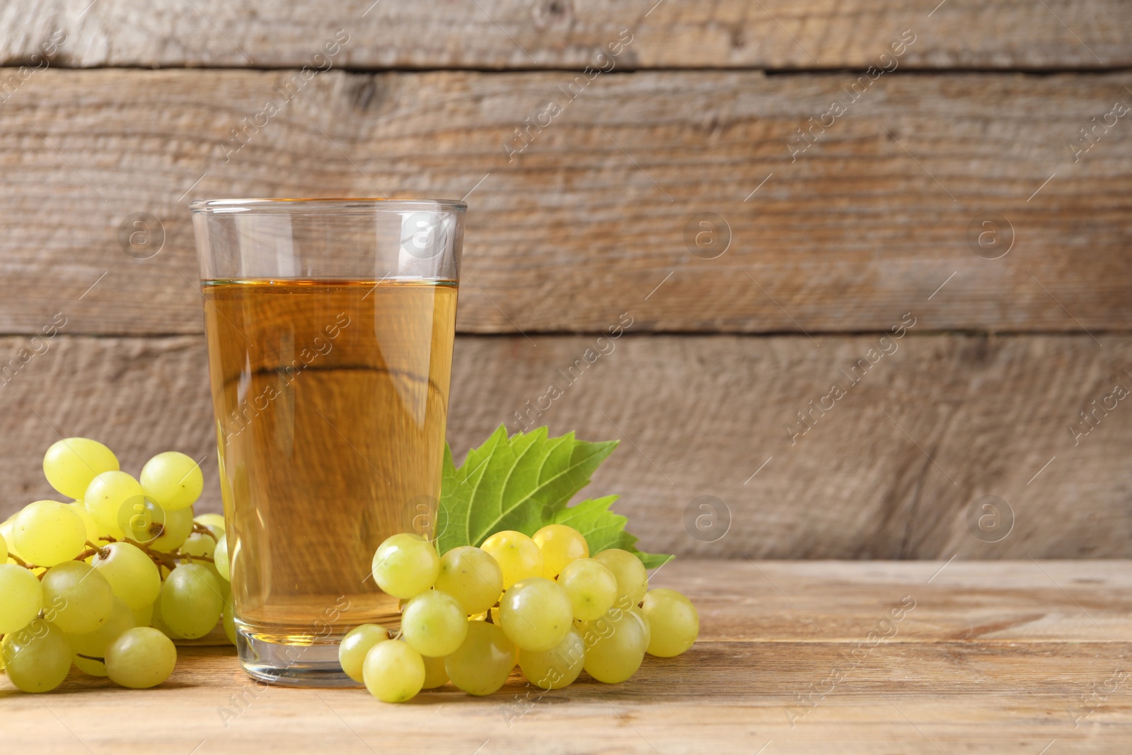 Photo of Tasty juice in glass and fresh grapes on wooden table, space for text