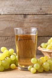 Tasty juice in glass and fresh grapes on wooden table