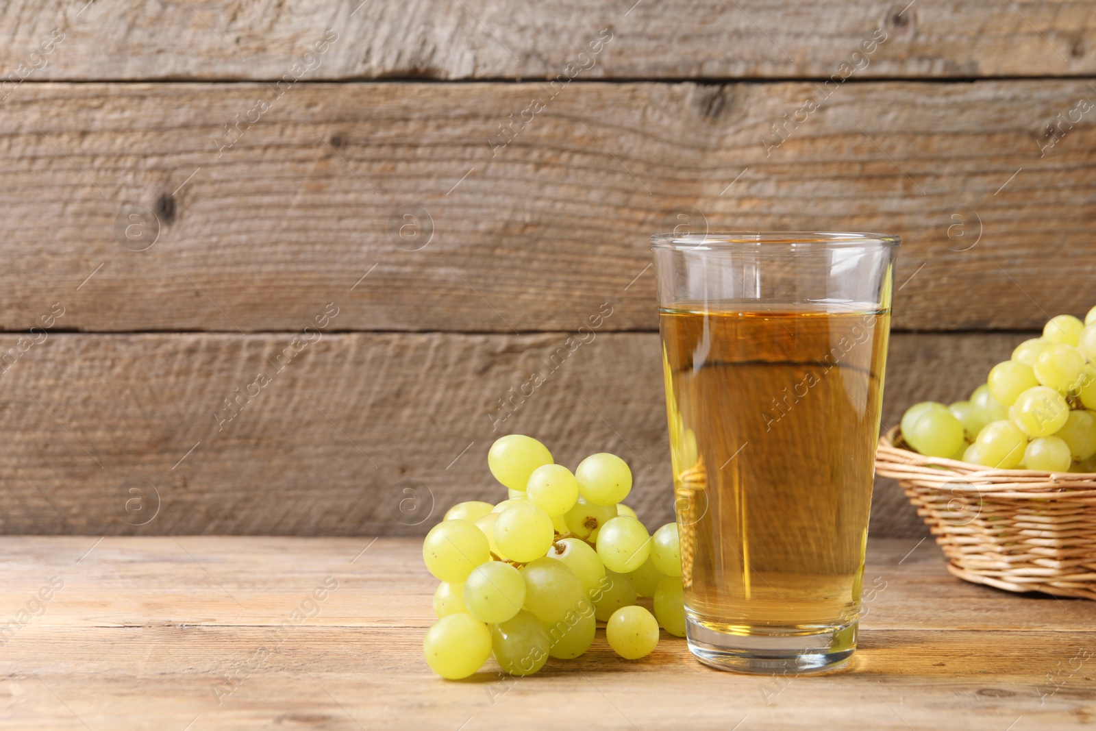 Photo of Tasty juice in glass and fresh grapes on wooden table, space for text