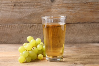 Tasty juice in glass and fresh grapes on wooden table