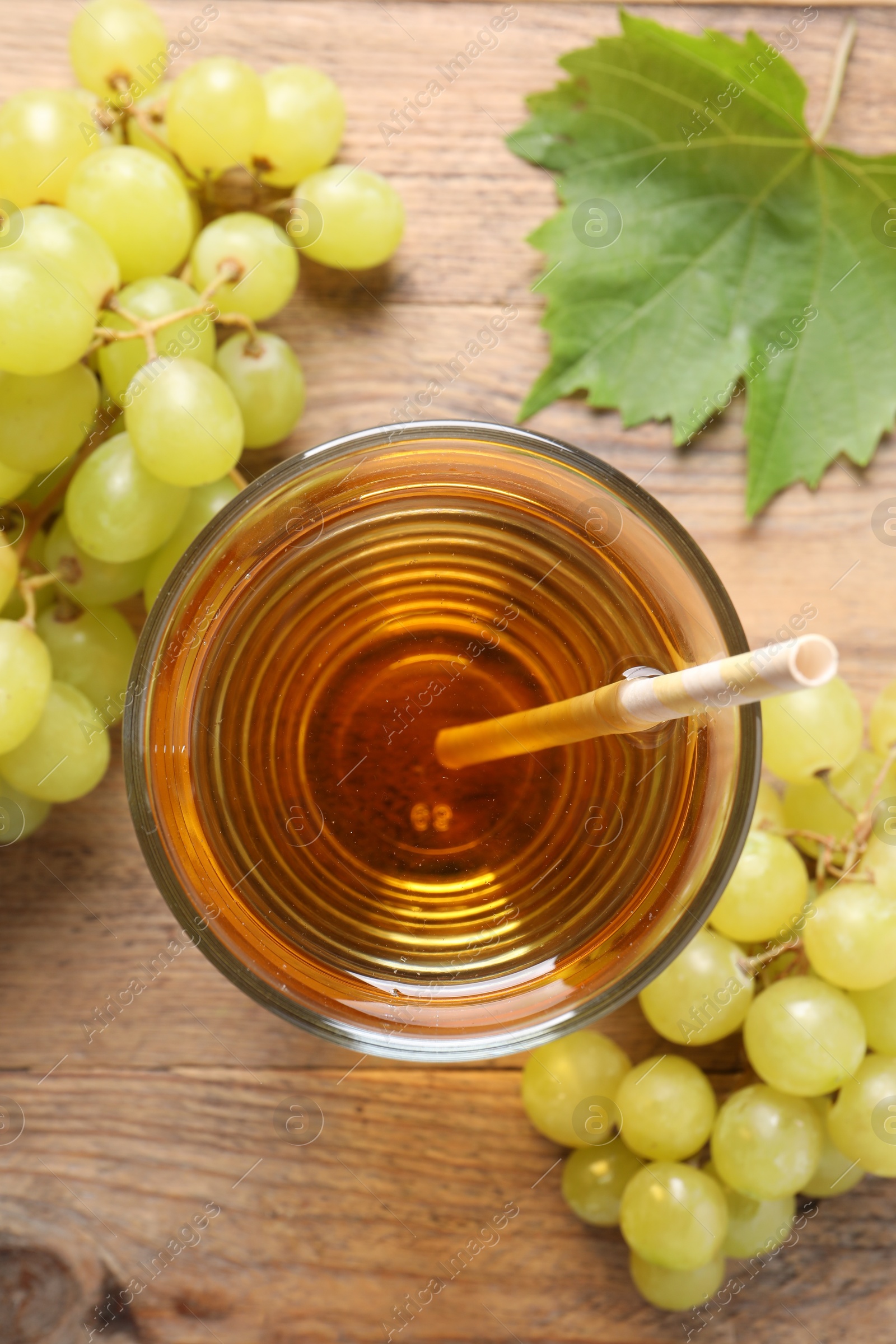 Photo of Tasty juice in glass, fresh grapes and leaf on wooden table, top view