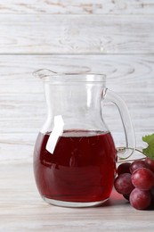 Photo of Tasty grape juice in jar and berries on light wooden table