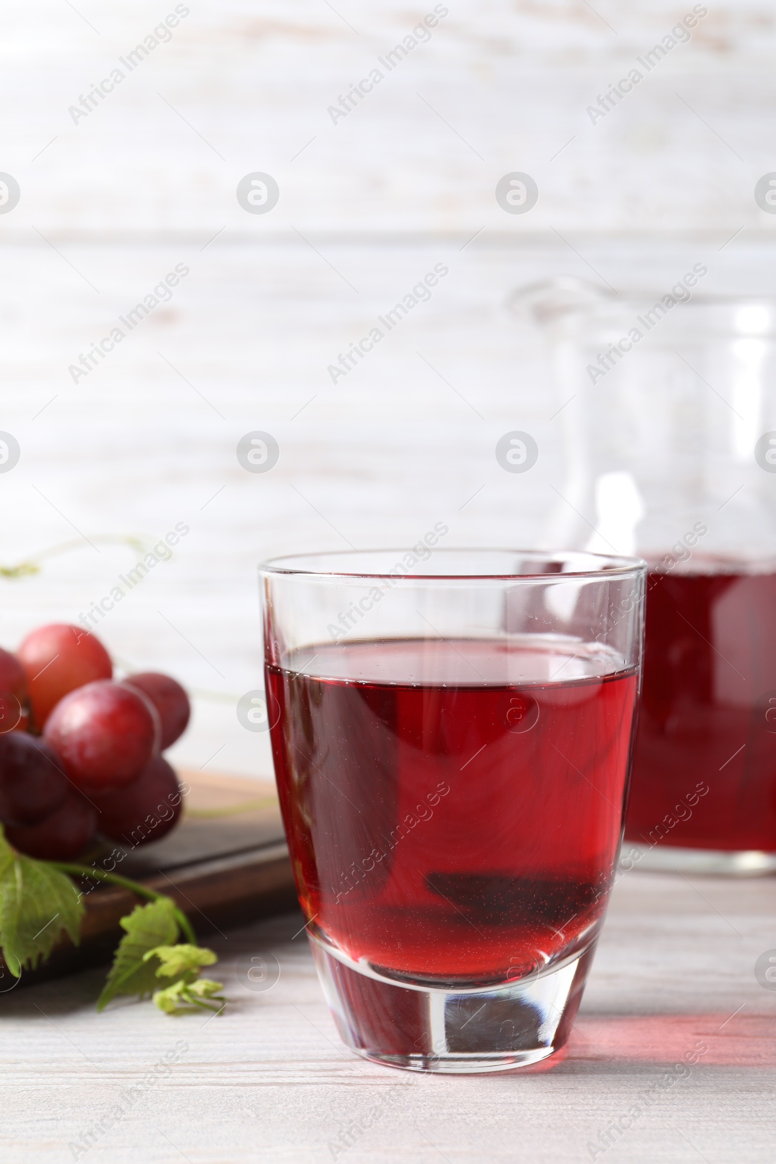 Photo of Tasty grape juice in glass, leaves and berries on light wooden table