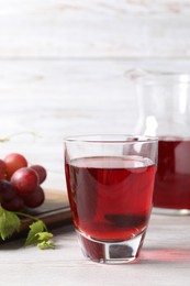 Photo of Tasty grape juice in glass, leaves and berries on light wooden table