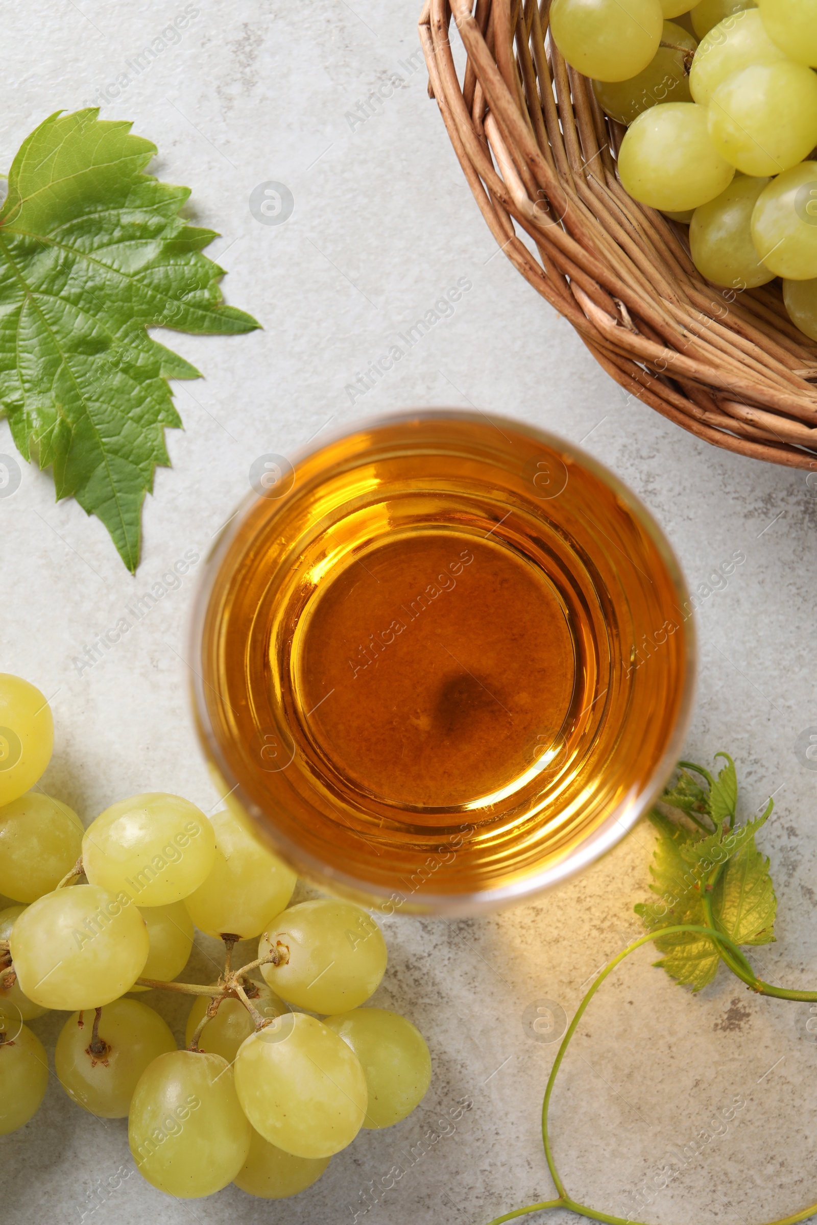 Photo of Tasty grape juice in glass, leaves and berries on light textured table, flat lay