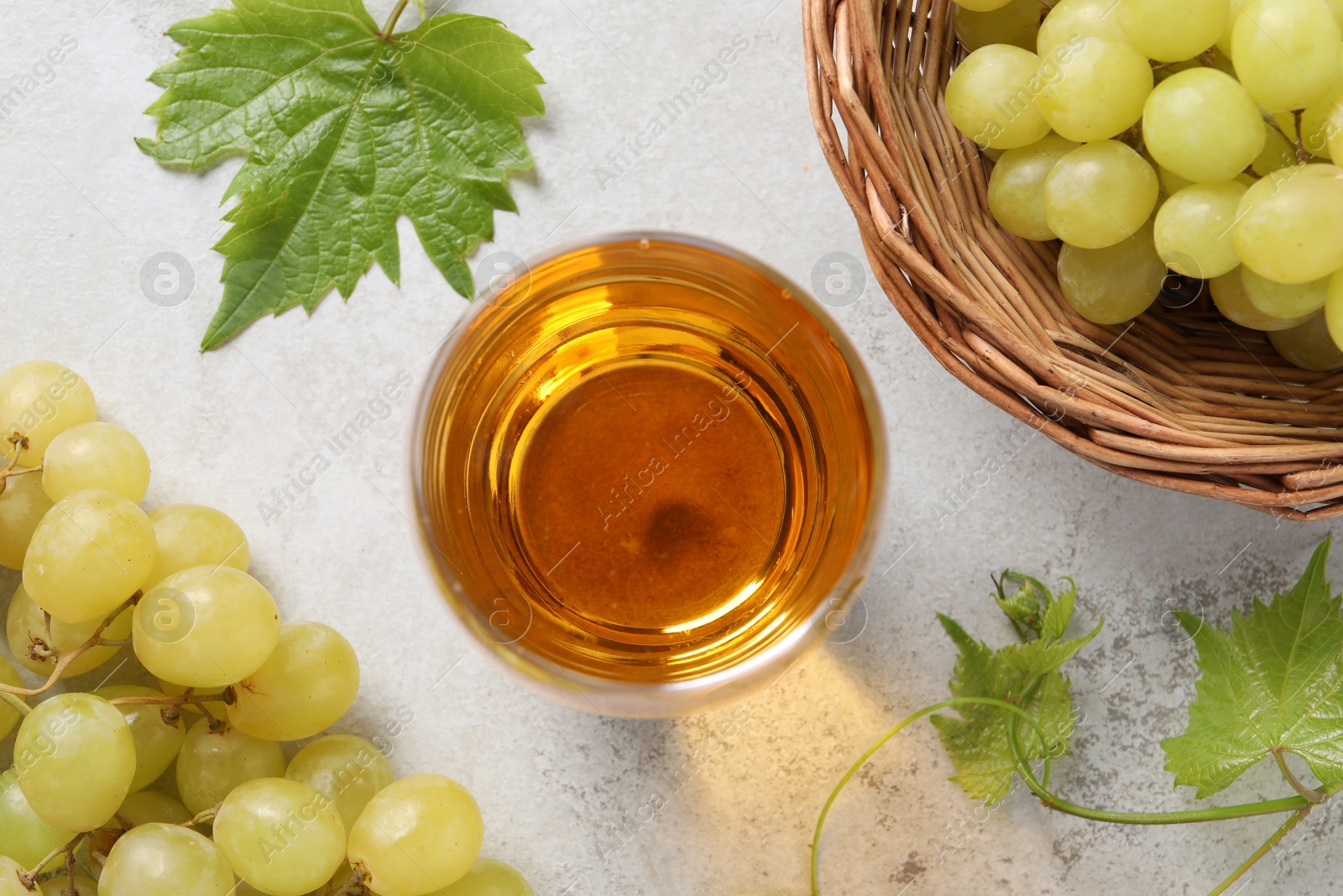 Photo of Tasty grape juice in glass, leaves and berries on light textured table, flat lay