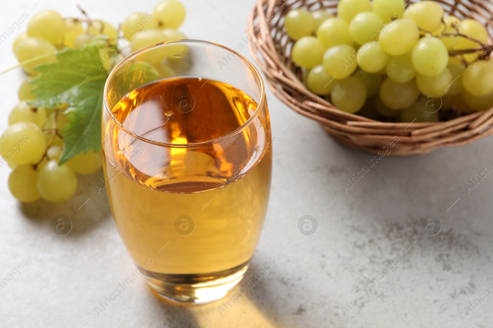 Photo of Tasty grape juice in glass and berries on light textured table, closeup