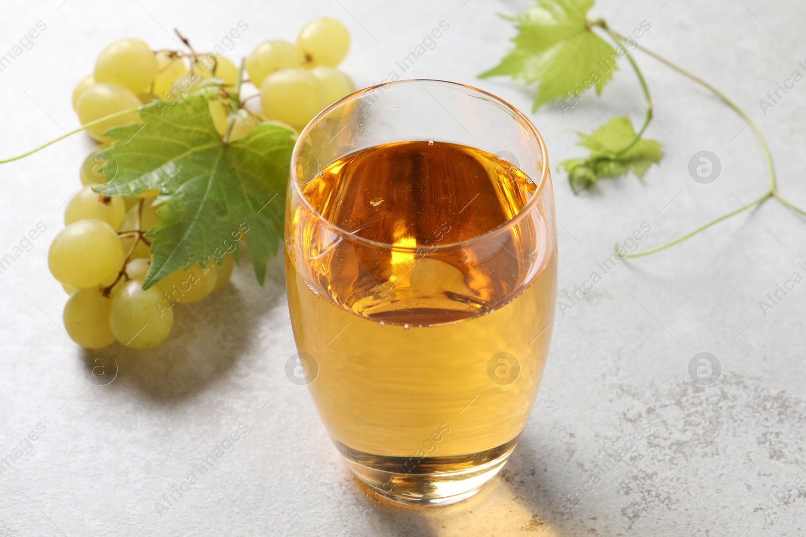 Photo of Tasty grape juice in glass, leaves and berries on light textured table, closeup