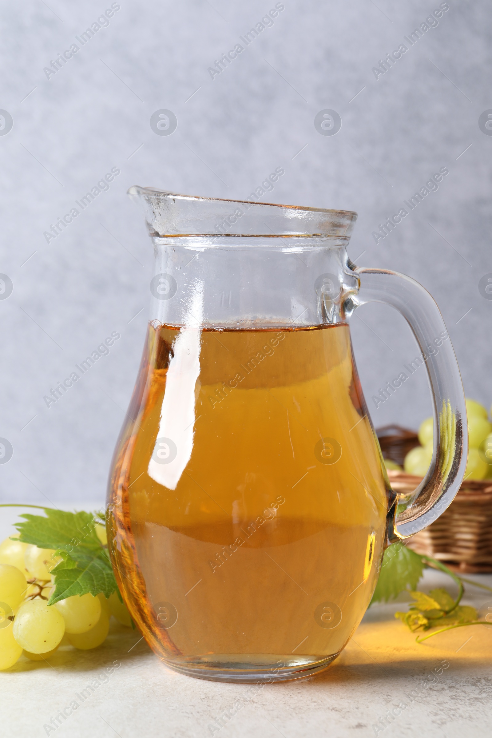 Photo of Tasty grape juice in jar and berries on light textured table, closeup