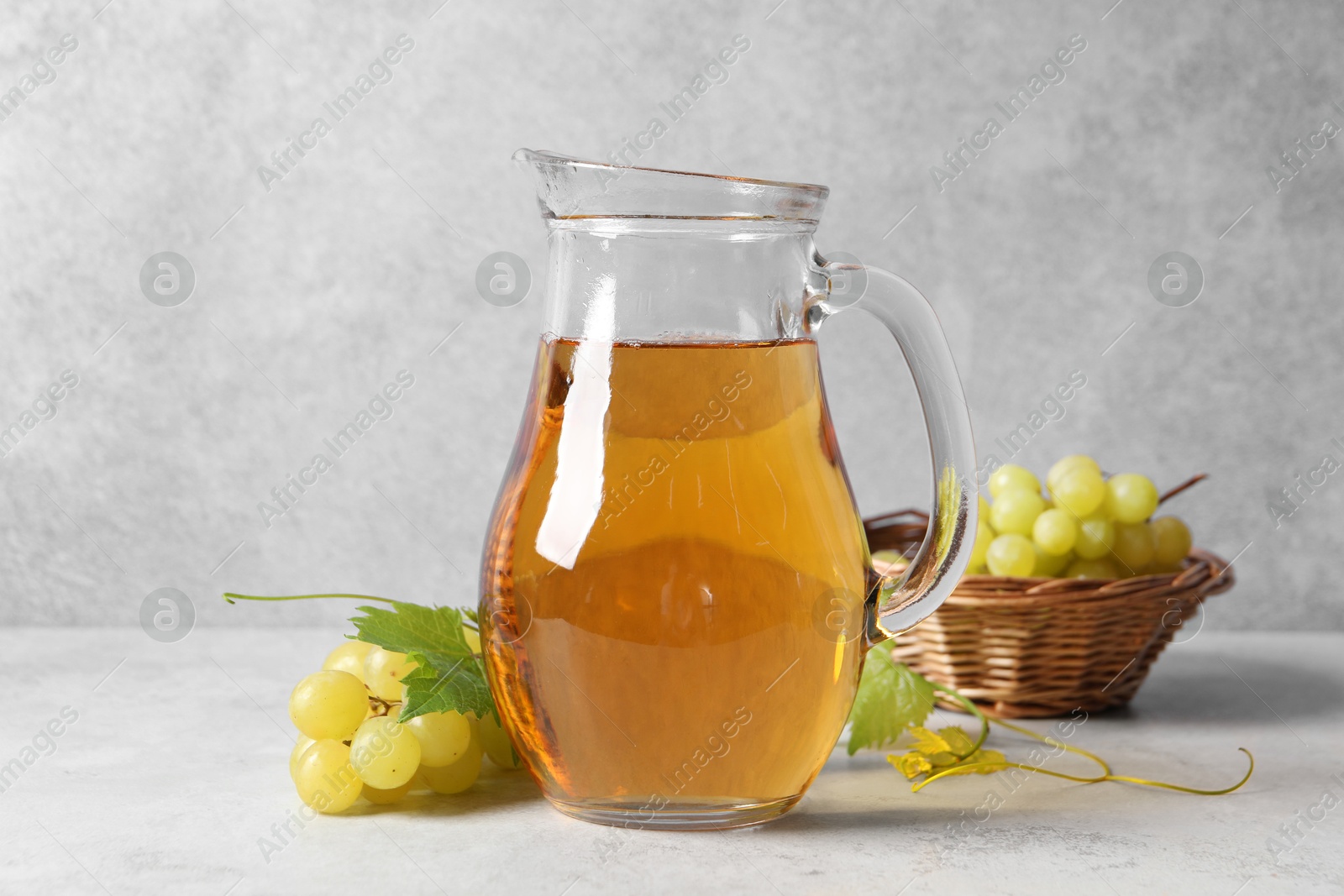 Photo of Tasty grape juice in jar and berries on light textured table, closeup