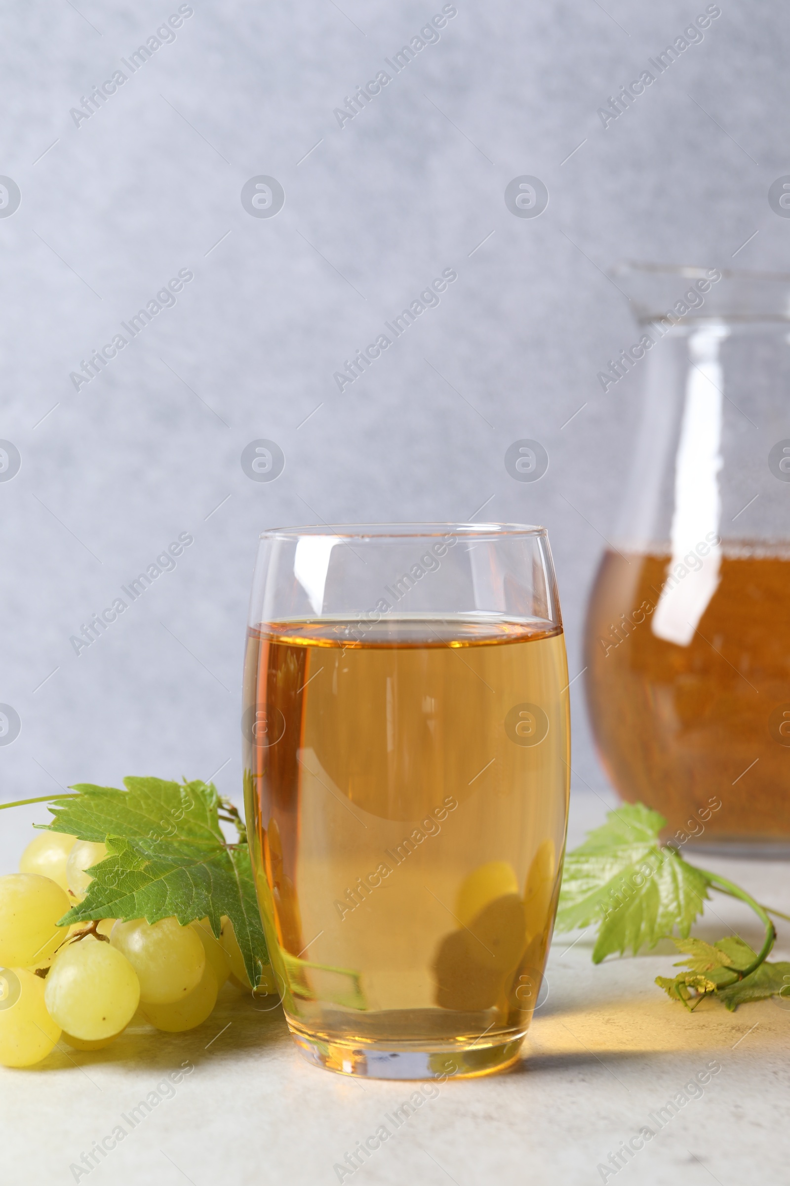 Photo of Tasty grape juice in glass, leaves and berries on light table