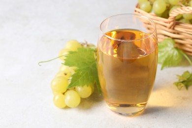 Photo of Tasty grape juice in glass, leaves and berries on light table, closeup