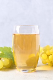 Tasty grape juice in glass, leaf and berries on light textured table, closeup